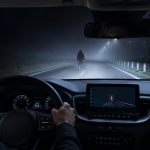 Driver approaching a pedestrian on a foggy night with dashboard pedestrian detection display visible