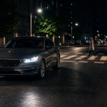 Luxury sedan driving at night on a city street as a pedestrian crosses ahead