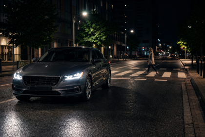 Luxury sedan driving at night on a city street as a pedestrian crosses ahead