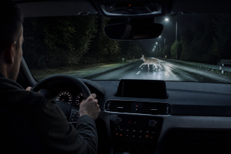 Thermal night vision camera display in a car showing heat signatures on a dark road